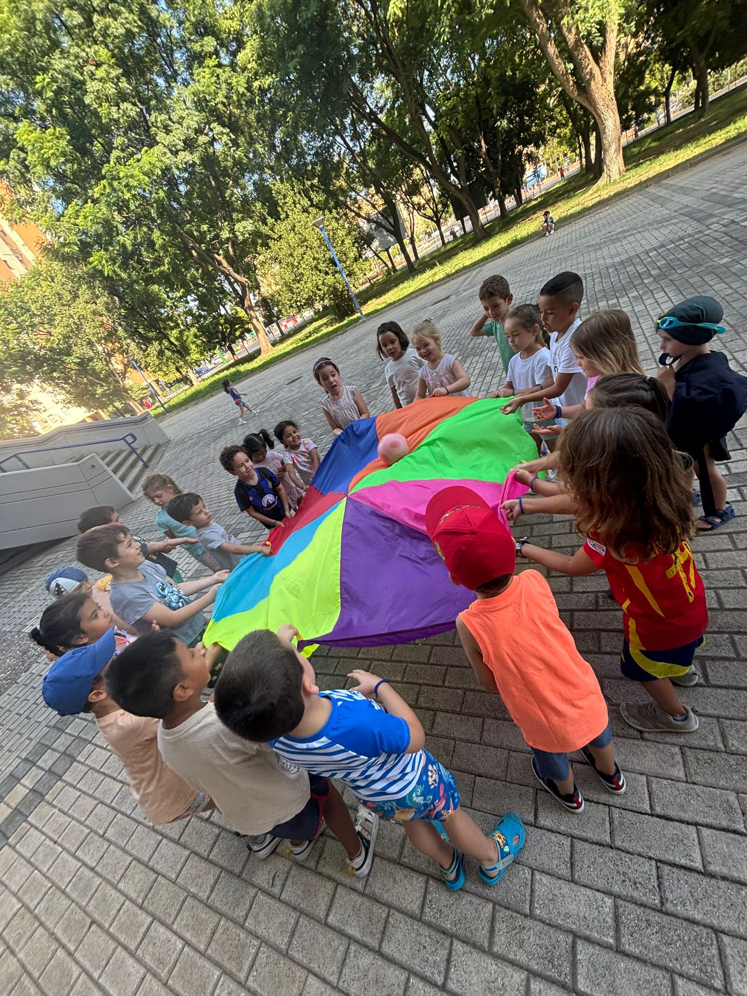 Niños jugando con paracaídas de colores en el parque durante el campus Atlantis